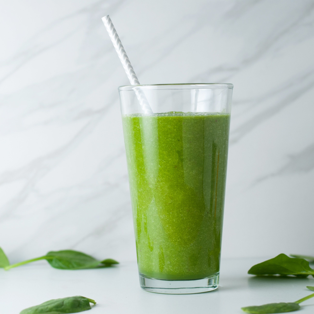 A Glowing Green Smoothie and spinach leaves on a kitchen counter.