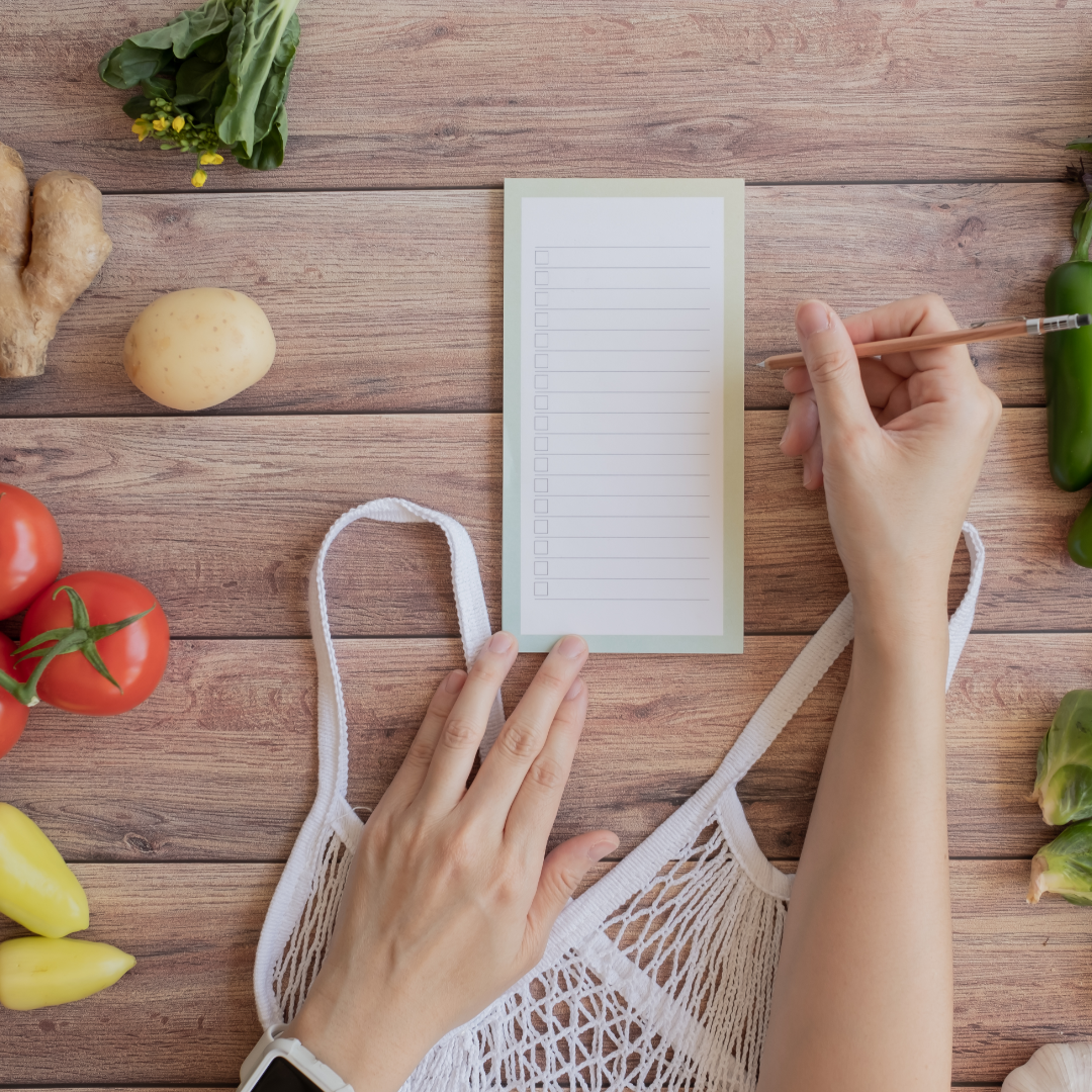 A woman making a grocery list on a table full of healthy produce.