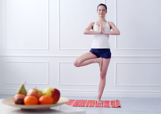 Healthy young woman practicing yoga near a bowl of fruit.