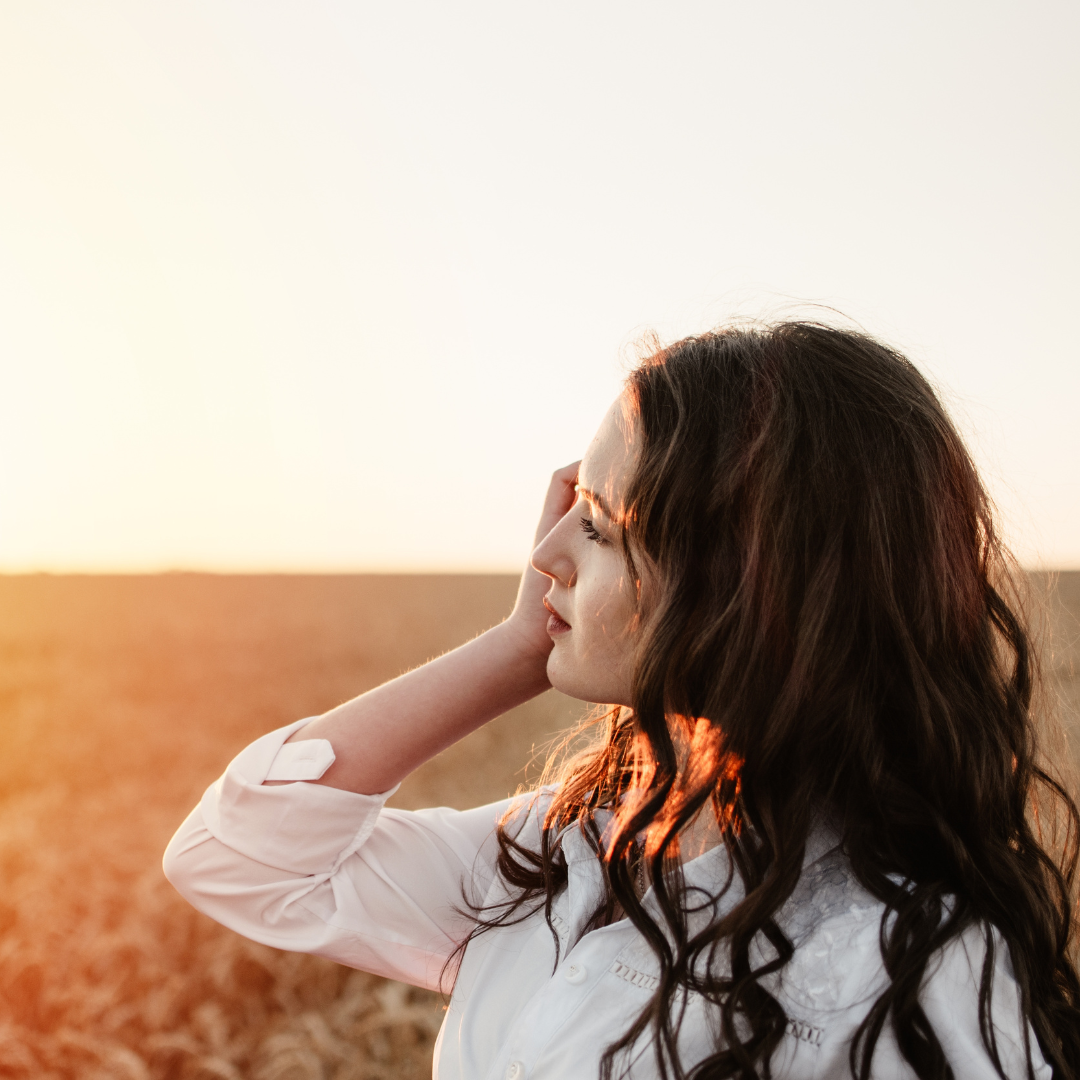 A young woman watching the sun set in a wheat field.