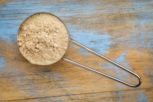 maca root powder on a metal measuring scoop against painted wood