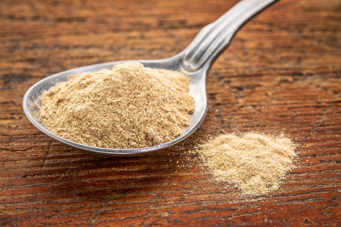 maca root powder on a tablespoon against rustic wood - superfood