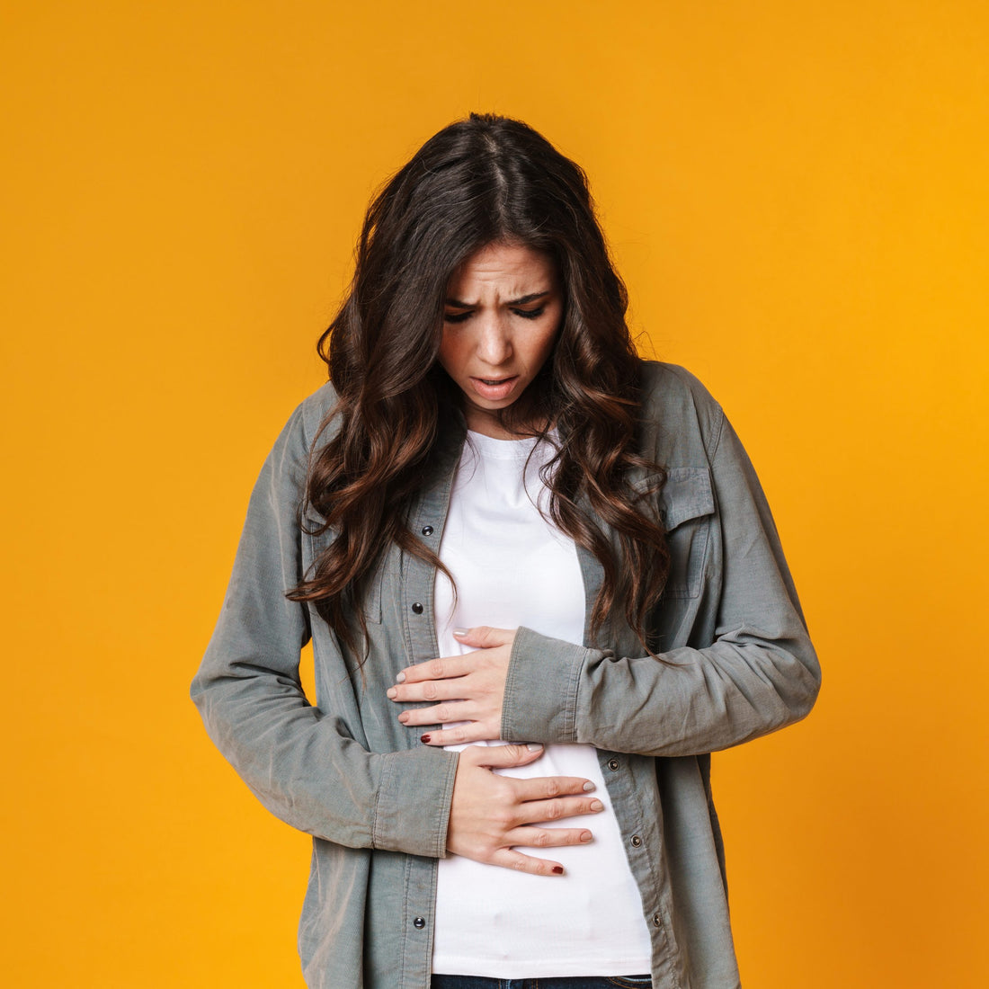Young woman clutches her stomach with uncomfortable gas and bloating from an unhealthy gut.