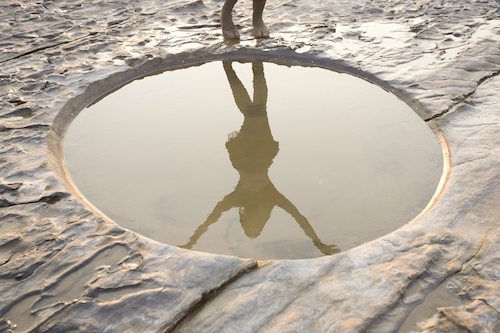 Picture of large puddle with female shadow reflecting in water. 