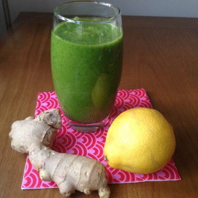 Picture of a green smoothie with a lemon and fresh ginger next to it