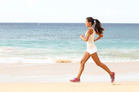 Fit young woman running along the edge of the surf on a sunny tropical beach in her sportswear with her long hair. Female runner exercising with copyspace