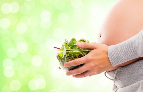 Picture of a young and pregnant woman with a fresh green salad.