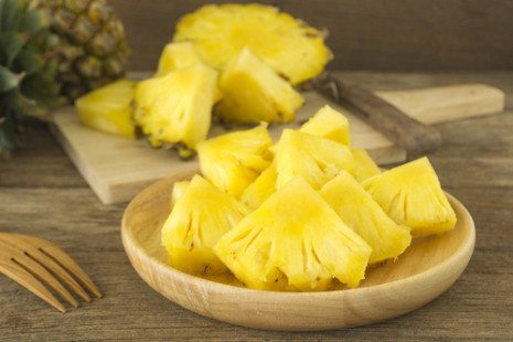 Picture of pineapple and pineapple slices on wood table.