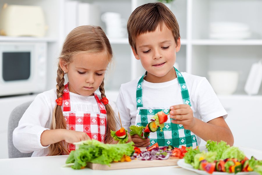 Kids with aprons preparing a healthy vegetables meal in the kitchen