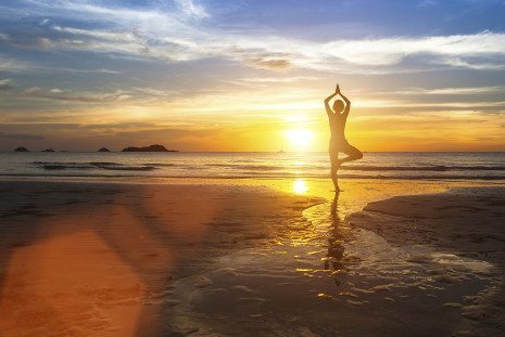 Silhouette of woman standing at yoga pose on the beach during am