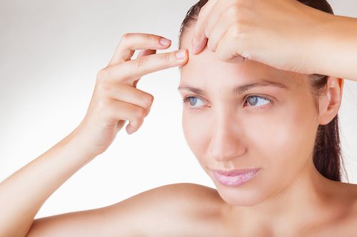 Picture of young woman squeezing pimple on her forehead on white background