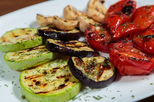 Grilled vegetables on a white plate. Zucchini, tomatoes, peppers grilled.