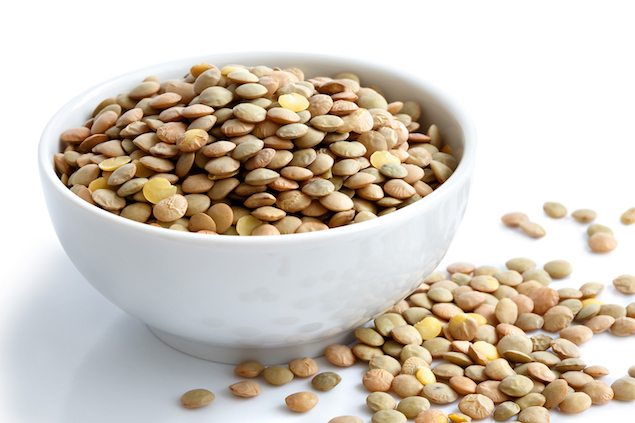 White Ceramic Bowl Of Green Uncooked Lentils Isolated On White In Perspective. Spilled Lentils.