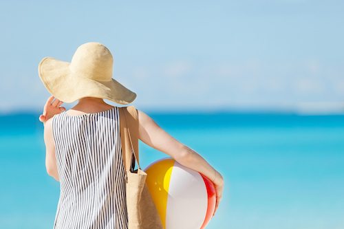 Picture of a woman at the beach back view holding beach ball and bag