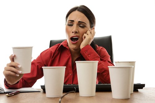 Picture of woman struggling to stay awake at ther desk with several cups of coffee.