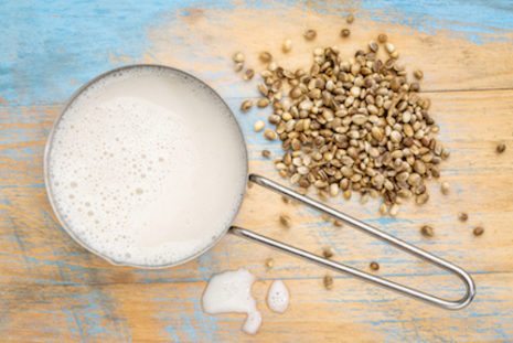 Picture of hemp milk in measuring cup with seeds against wooden background.
