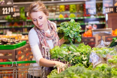 Portrait of beautiful young woman choosing green leafy vegetables in grocery store. Concept of healthy food shopping
