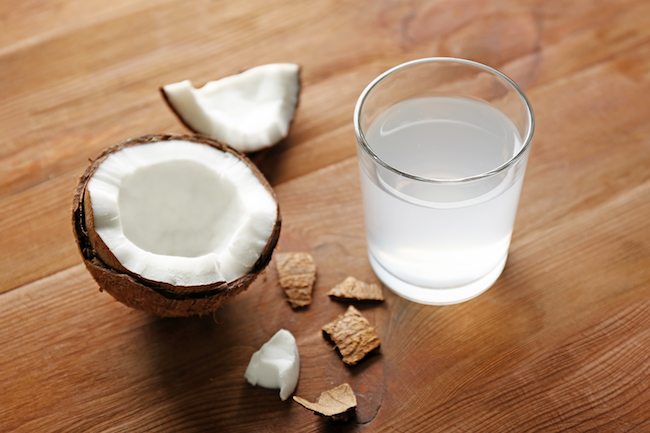 Glass of coconut water and fresh nut on wooden background