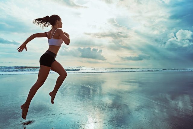 Active sporty woman run along ocean surf by water pool to keep fit and health. Sunset black sand beach background with sun. Woman fitness jogging workout and sport activity on summer family holiday.
