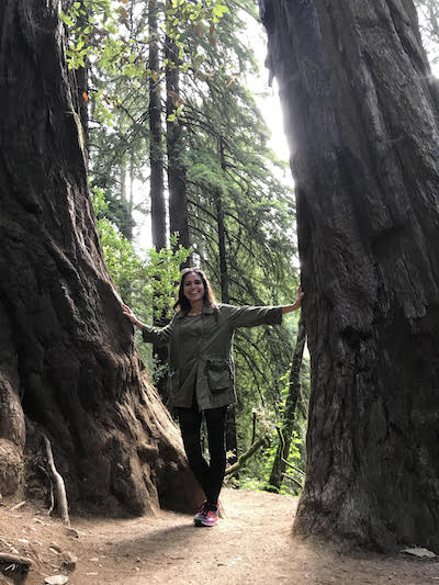 Picture of Kimberly Snyder standing next to a big tree in the forest. 