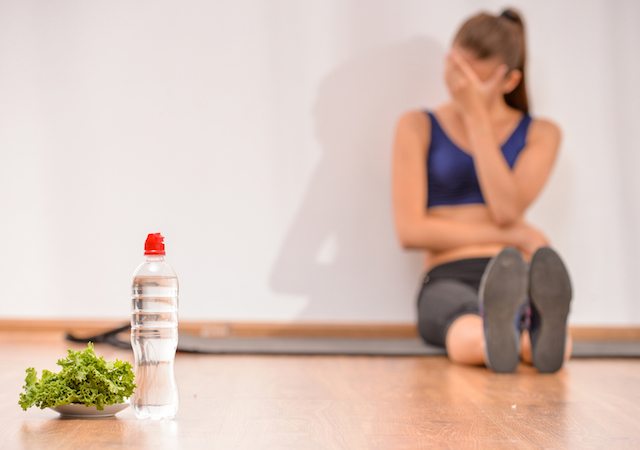 Young sadness woman is sitting on the floor. Focus on salad and bottle of water.
