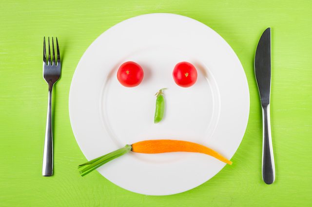 Sad face of vegetables the concept of dietary restrictions healthy lifestyle diet weight loss anti-obesity healthy diet. Two tomatoes peas in a pod and carrots on a plate knife fork.