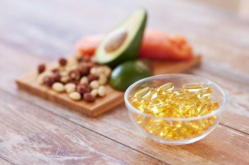 Picture of healthy eating, diet and omega 3 nutritional supplements concept - close up of cold liver oil capsules in glass bowl and food on table.