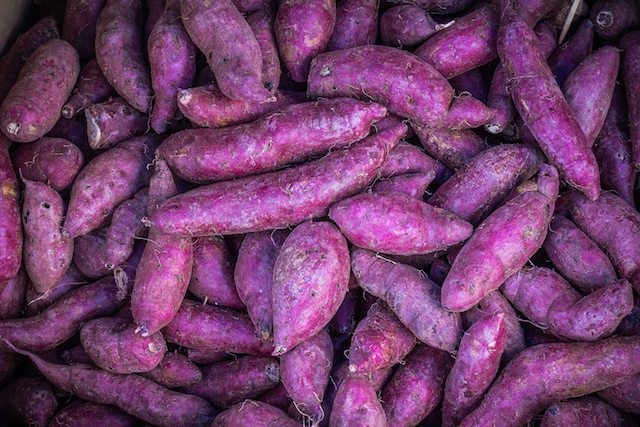 Many piles of purple sweet potato in vegetable market.