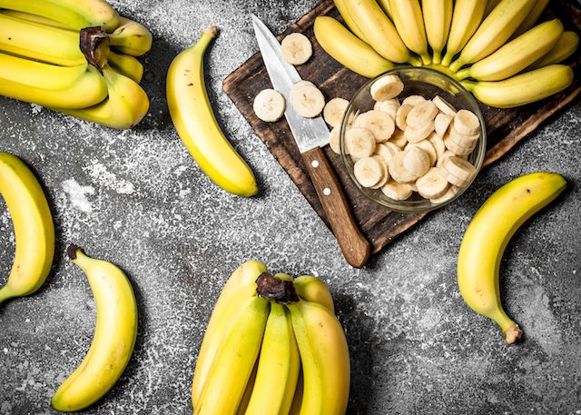 Fresh bananas with pieces of sliced bananas in a bowl. On rustic background.