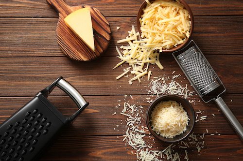 Graters, bowls with cheese and cutting board on wooden background