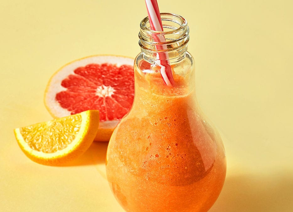 Orange smoothies with citrus, carrots, sea buckthorn and almonds on an orange paper background
