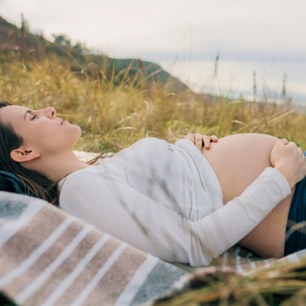 Young Pregnant Woman Relaxing Outside in Grassy Field
