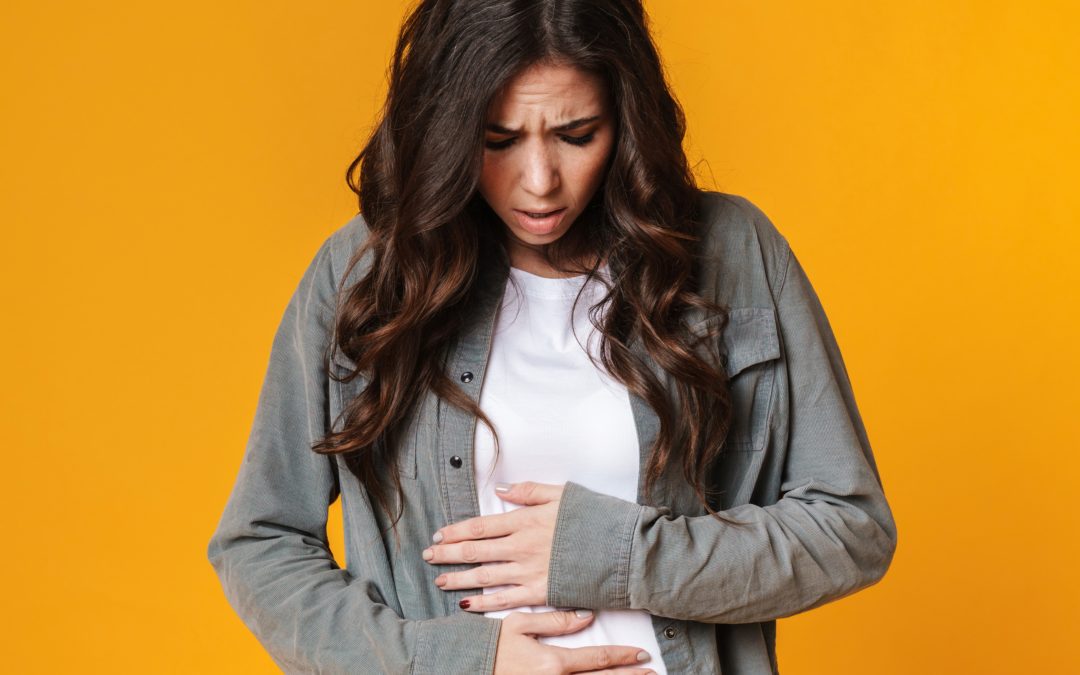 Young woman clutches her stomach with uncomfortable gas and bloating from an unhealthy gut.