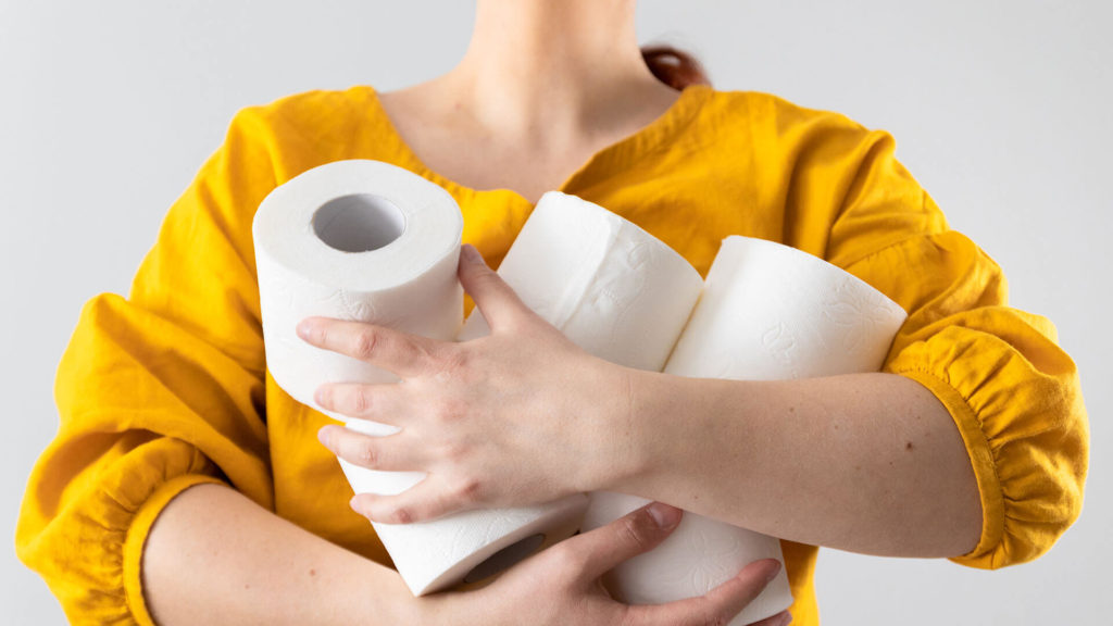 A woman in a yellow shirt holding rolls of toilet paper