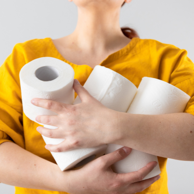 A woman in a yellow shirt holding rolls of toilet paper.