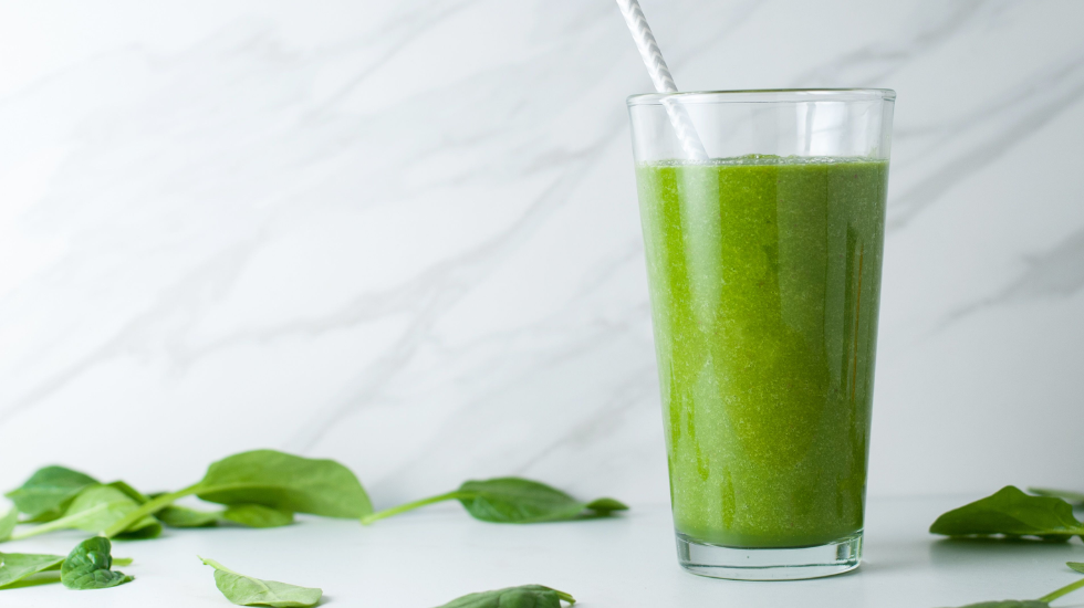 A Glowing Green Smoothie and spinach leaves on a kitchen counter.