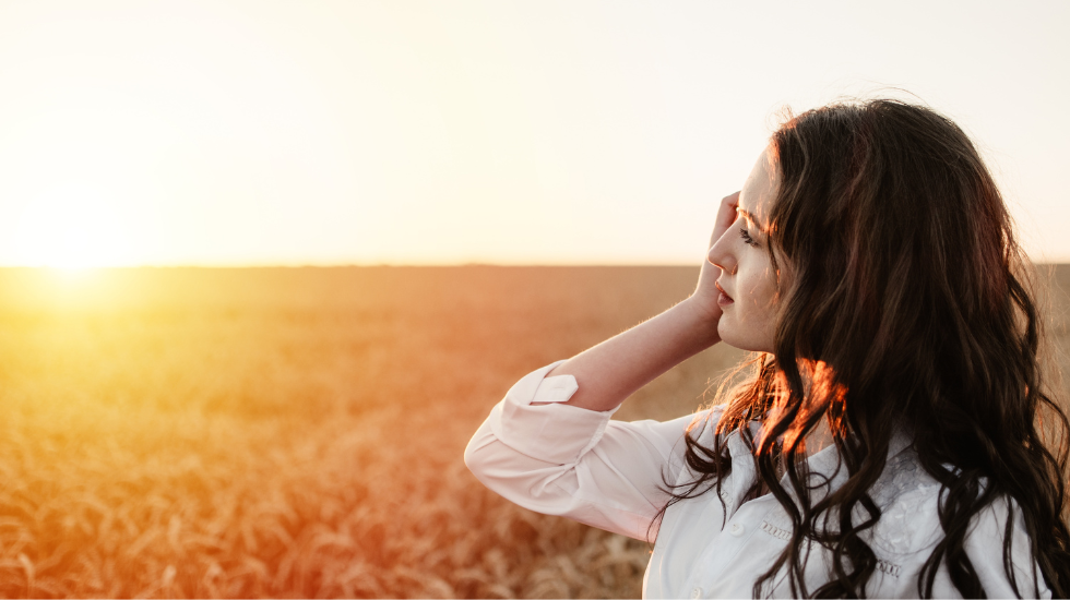 A young woman watching the sun set in a wheat field.