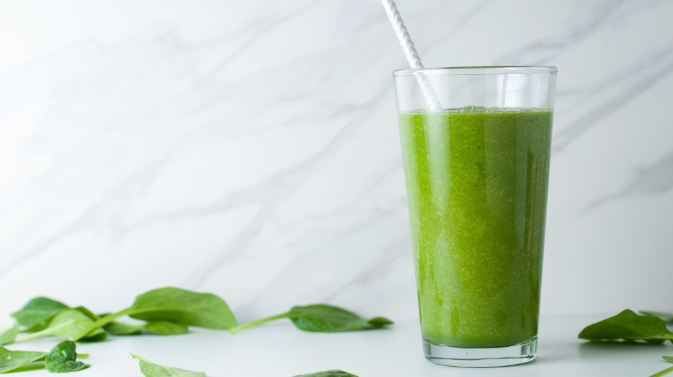 A glowing green smoothie surrounded by spinach leaves.