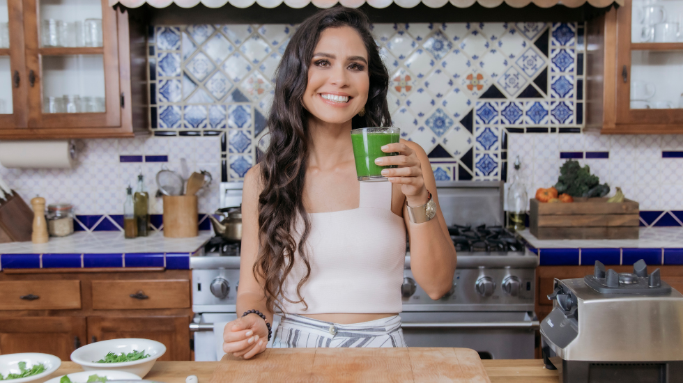 Kimberly Snyder holding a glowing green smoothie in her kitchen.