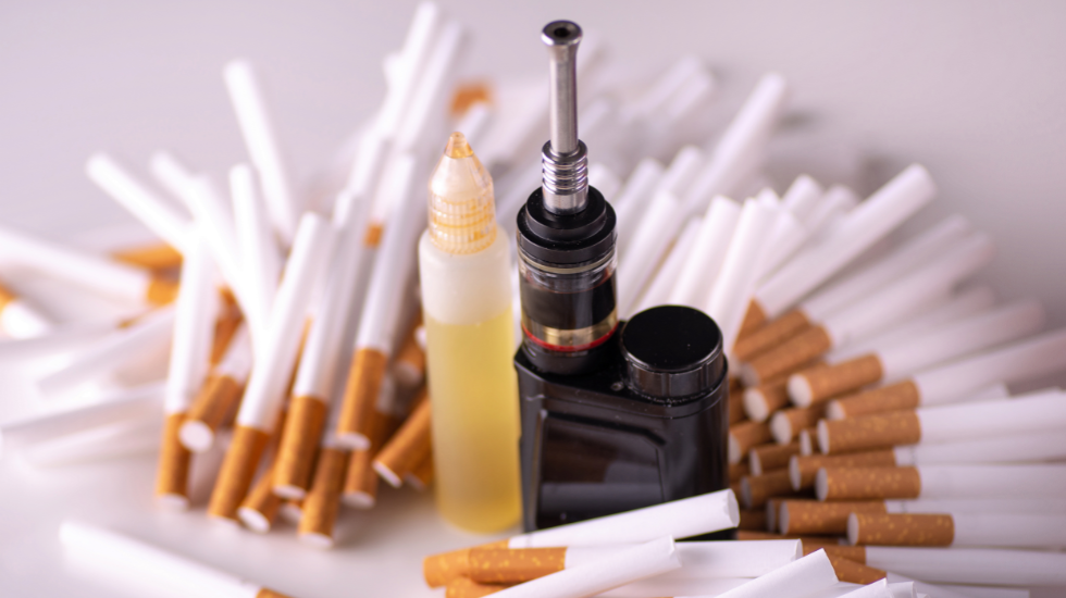 A vape pen and vape juice surrounded by cigarettes.